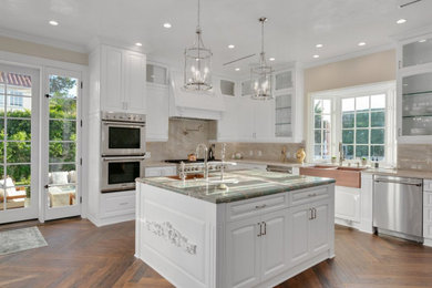 Example of a large transitional u-shaped dark wood floor and multicolored floor enclosed kitchen design in Los Angeles with a farmhouse sink, shaker cabinets, white cabinets, marble countertops, beige backsplash, marble backsplash, stainless steel appliances, two islands and turquoise countertops