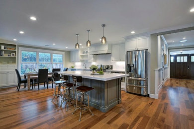 Open concept kitchen - mid-sized transitional single-wall medium tone wood floor open concept kitchen idea in San Francisco with a farmhouse sink, shaker cabinets, gray cabinets, quartz countertops, white backsplash, subway tile backsplash, stainless steel appliances and an island