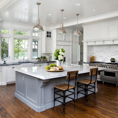 Large trendy l-shaped dark wood floor and brown floor kitchen photo in San Francisco with a farmhouse sink, beaded inset cabinets, white cabinets, marble countertops, white backsplash, stone slab backsplash, paneled appliances and an island