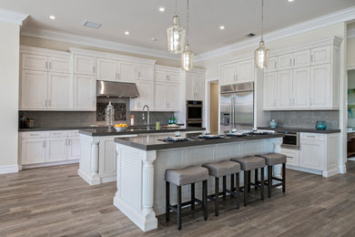 Open concept kitchen - large transitional l-shaped medium tone wood floor open concept kitchen idea in Miami with an undermount sink, recessed-panel cabinets, white cabinets, solid surface countertops, gray backsplash, subway tile backsplash, stainless steel appliances and an island