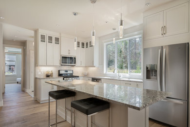 Example of a mid-sized transitional l-shaped light wood floor and brown floor eat-in kitchen design in Vancouver with an undermount sink, shaker cabinets, white cabinets, granite countertops, white backsplash, subway tile backsplash, stainless steel appliances, an island and white countertops