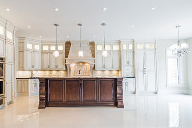 Example of a large classic l-shaped marble floor eat-in kitchen design in Toronto with an undermount sink, raised-panel cabinets, distressed cabinets, granite countertops, beige backsplash, stone tile backsplash, paneled appliances and an island