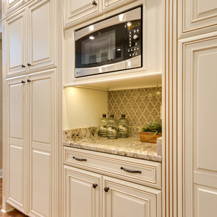 Photo of a mid-sized traditional u-shaped eat-in kitchen in Atlanta with an undermount sink, raised-panel cabinets, granite benchtops, beige splashback, stainless steel appliances, light hardwood floors, with island, beige cabinets, porcelain splashback, brown floor and beige benchtop.