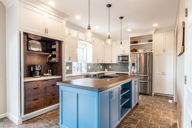 Example of a mid-sized country u-shaped vinyl floor and brown floor eat-in kitchen design in Philadelphia with a farmhouse sink, flat-panel cabinets, white cabinets, wood countertops, gray backsplash, ceramic backsplash, stainless steel appliances, an island and brown countertops