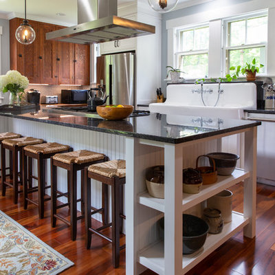 Inspiration for a country l-shaped medium tone wood floor and brown floor kitchen remodel in Boston with a farmhouse sink, recessed-panel cabinets, medium tone wood cabinets, stainless steel appliances and black countertops