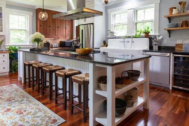 Inspiration for a country l-shaped medium tone wood floor and brown floor kitchen remodel in Boston with a farmhouse sink, recessed-panel cabinets, medium tone wood cabinets, stainless steel appliances and black countertops