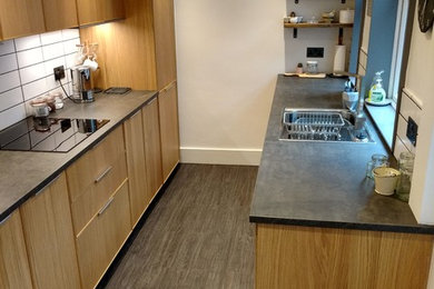 Photo of a small modern galley enclosed kitchen in Other with a single-bowl sink, beaded cabinets, medium wood cabinets, concrete worktops, white splashback, ceramic splashback, black appliances, laminate floors, no island and grey floors.