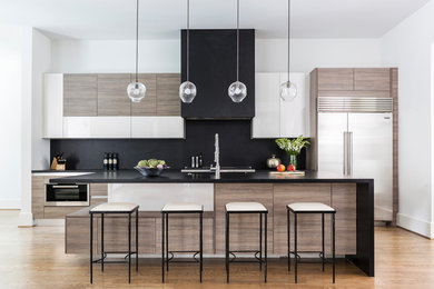 Zweizeilige Moderne Küche mit flächenbündigen Schrankfronten, hellbraunen Holzschränken, Küchenrückwand in Schwarz, Küchengeräten aus Edelstahl, braunem Holzboden, Kücheninsel, braunem Boden und schwarzer Arbeitsplatte in Houston
