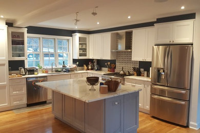 Large classic l-shaped open plan kitchen in New York with a submerged sink, shaker cabinets, white cabinets, stainless steel appliances, light hardwood flooring, an island, beige floors, marble worktops and white worktops.