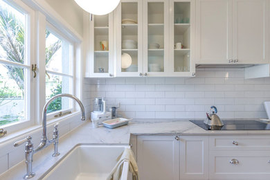 Inspiration for a mid-sized timeless l-shaped medium tone wood floor and brown floor kitchen remodel in Auckland with a farmhouse sink, shaker cabinets, white cabinets, granite countertops, white backsplash, ceramic backsplash, stainless steel appliances, no island and gray countertops