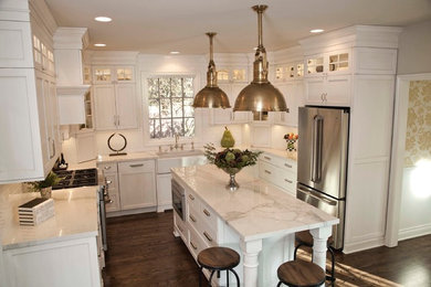 This is an example of a traditional u-shaped kitchen/diner in Detroit with a belfast sink, shaker cabinets, white cabinets, marble worktops, white splashback, metro tiled splashback, stainless steel appliances, dark hardwood flooring and an island.