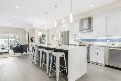 Large minimalist single-wall light wood floor open concept kitchen photo in Vancouver with white cabinets, quartzite countertops, blue backsplash, glass tile backsplash, stainless steel appliances and an island