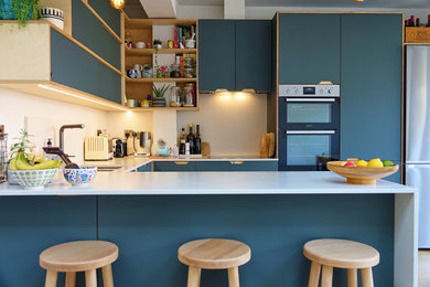 Design ideas for a contemporary u-shaped kitchen in Sussex with a submerged sink, flat-panel cabinets, blue cabinets, light hardwood flooring, a breakfast bar, beige floors and white worktops.