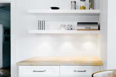 Modelo de cocina moderna pequeña con encimera de madera, salpicadero blanco, electrodomésticos de acero inoxidable y suelo de madera en tonos medios