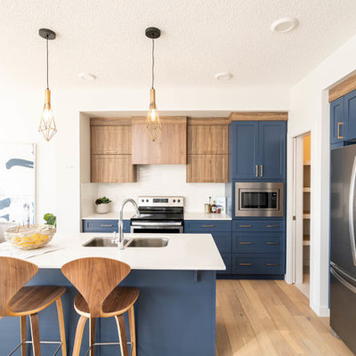 Example of a small trendy l-shaped light wood floor and beige floor open concept kitchen design in Edmonton with shaker cabinets, blue cabinets, white backsplash, stainless steel appliances, an island, white countertops, an undermount sink, marble countertops and ceramic backsplash