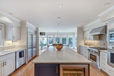 Example of a transitional galley medium tone wood floor and brown floor eat-in kitchen design in Dallas with an undermount sink, shaker cabinets, white cabinets, beige backsplash, stainless steel appliances and an island
