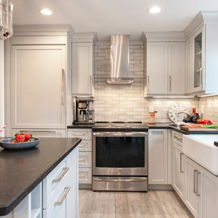 Inspiration for a mid-sized transitional l-shaped kitchen in Bridgeport with a farmhouse sink, recessed-panel cabinets, grey cabinets, granite benchtops, grey splashback, ceramic splashback, stainless steel appliances, vinyl floors, black benchtop and beige floor.