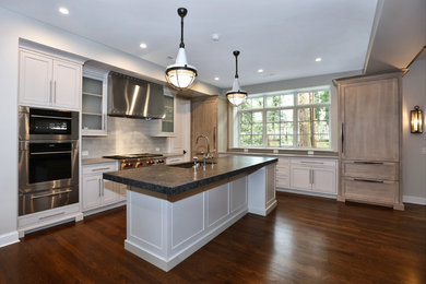 Inredning av ett klassiskt mellanstort kök, med en undermonterad diskho, luckor med profilerade fronter, vita skåp, granitbänkskiva, vitt stänkskydd, rostfria vitvaror, mörkt trägolv, en köksö och brunt golv