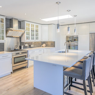 Expansive beach style galley open plan kitchen in Toronto with a double-bowl sink, beaded inset cabinets, white cabinets, laminate benchtops, grey splashback, stone tile splashback, stainless steel appliances, light hardwood floors and with island.