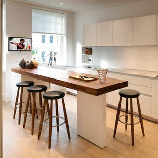 Photo of a mid-sized contemporary single-wall kitchen in London with an integrated sink, white splashback, medium hardwood floors, with island, flat-panel cabinets, white cabinets, stainless steel benchtops and glass sheet splashback.