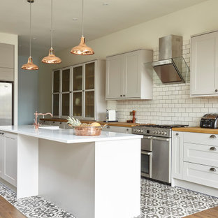 Classic galley kitchen in London with a belfast sink, shaker cabinets, white cabinets, wood worktops, white splashback, metro tiled splashback, stainless steel appliances, an island, multi-coloured floors and brown worktops.