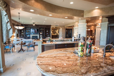 ラスベガスにある高級な広いおしゃれなキッチン (ドロップインシンク、濃色木目調キャビネット、シルバーの調理設備、大理石の床) の写真