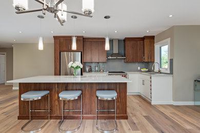 Large trendy l-shaped medium tone wood floor and brown floor eat-in kitchen photo in Calgary with a double-bowl sink, flat-panel cabinets, dark wood cabinets, quartz countertops, blue backsplash, glass tile backsplash, stainless steel appliances and an island
