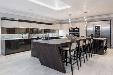 This is an example of an expansive contemporary l-shaped open plan kitchen in Buckinghamshire with flat-panel cabinets, dark wood cabinets, granite worktops, multi-coloured splashback, stone slab splashback, stainless steel appliances and multiple islands.