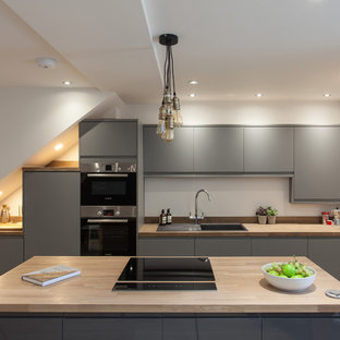 Inspiration for a small contemporary galley kitchen in London with a built-in sink, flat-panel cabinets, grey cabinets, wood worktops, white splashback, light hardwood flooring, an island and beige floors.