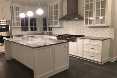 Kitchen - large transitional u-shaped black floor kitchen idea with an undermount sink, recessed-panel cabinets, white cabinets, quartzite countertops, white backsplash, ceramic backsplash, stainless steel appliances, an island and gray countertops