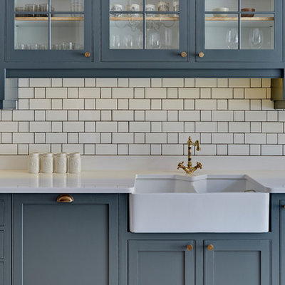 Example of a mid-sized transitional galley light wood floor and brown floor open concept kitchen design in London with a farmhouse sink, shaker cabinets, white backsplash, ceramic backsplash, stainless steel appliances, gray cabinets, quartzite countertops, a peninsula and white countertops