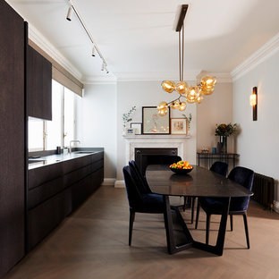 Design ideas for a medium sized contemporary single-wall kitchen/diner in London with an integrated sink, dark wood cabinets, granite worktops, black splashback, stainless steel appliances, no island, brown floors, black worktops, flat-panel cabinets and medium hardwood flooring.