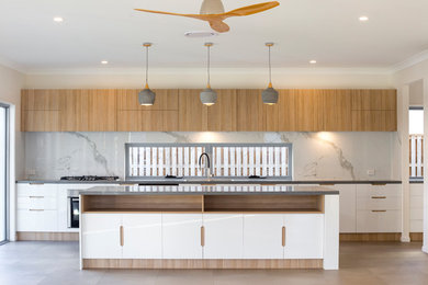 This is an example of a contemporary galley kitchen in Brisbane with flat-panel cabinets, white cabinets, stone slab splashback, stainless steel appliances, an island, beige floors and grey worktops.