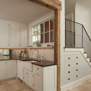 Réalisation d'une cuisine américaine chalet en L de taille moyenne avec un évier de ferme, un sol en travertin, un placard à porte plane, une crédence blanche, une crédence en carreau de céramique, des portes de placard blanches et un sol beige.