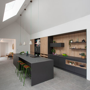 This is an example of a contemporary galley kitchen in West Midlands with flat-panel cabinets, black cabinets, beige splashback, wood splashback, black appliances, an island, grey floors and black worktops.