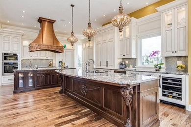 Eat-in kitchen - large traditional l-shaped medium tone wood floor and brown floor eat-in kitchen idea in Calgary with an undermount sink, raised-panel cabinets, white cabinets, gray backsplash, mosaic tile backsplash, two islands, granite countertops and stainless steel appliances