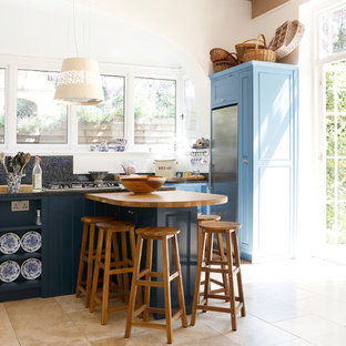 This is an example of a medium sized farmhouse kitchen in Kent with blue cabinets, shaker cabinets, black splashback, stainless steel appliances, beige floors and black worktops.