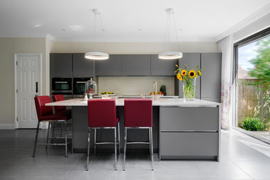 Design ideas for a medium sized contemporary kitchen in London with flat-panel cabinets, grey cabinets, composite countertops, beige splashback, glass sheet splashback, cement flooring, an island and grey floors.