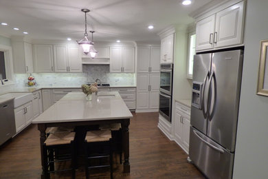 Large transitional u-shaped dark wood floor eat-in kitchen photo in Chicago with a farmhouse sink, raised-panel cabinets, white cabinets, quartz countertops, gray backsplash, stone tile backsplash, stainless steel appliances and an island