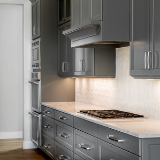 This is an example of a mid-sized arts and crafts galley open plan kitchen in Boise with recessed-panel cabinets, grey cabinets, granite benchtops, white splashback, stone tile splashback, medium hardwood floors and with island.