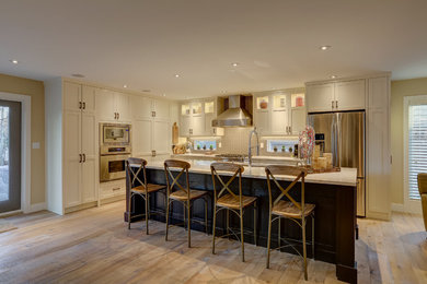 Photo of a large traditional l-shaped open plan kitchen in Calgary with a submerged sink, shaker cabinets, white cabinets, quartz worktops, beige splashback, mosaic tiled splashback, stainless steel appliances, medium hardwood flooring and an island.