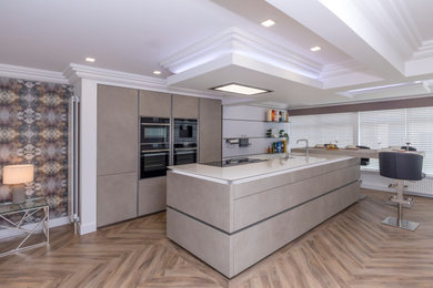 Large modern open plan kitchen in Glasgow with flat-panel cabinets, engineered stone countertops, black appliances, an island and white worktops.
