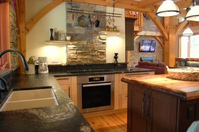 Example of a mid-sized mountain style u-shaped medium tone wood floor and beige floor eat-in kitchen design in Toronto with a double-bowl sink, recessed-panel cabinets, light wood cabinets, granite countertops, black backsplash, stone slab backsplash, stainless steel appliances and an island