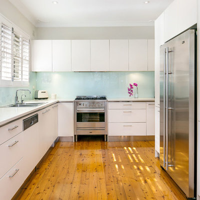 Enclosed kitchen - mid-sized contemporary l-shaped medium tone wood floor enclosed kitchen idea in Sydney with a double-bowl sink, white cabinets, limestone countertops, glass sheet backsplash, stainless steel appliances, flat-panel cabinets and blue backsplash