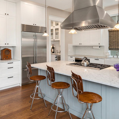 Country medium tone wood floor kitchen photo in Seattle with a farmhouse sink, shaker cabinets, white cabinets, marble countertops, white backsplash, subway tile backsplash, stainless steel appliances and an island