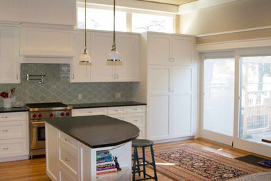 Example of a mid-sized arts and crafts l-shaped medium tone wood floor open concept kitchen design in Seattle with an undermount sink, recessed-panel cabinets, white cabinets, soapstone countertops, blue backsplash, glass tile backsplash, stainless steel appliances and an island