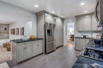 Inspiration for a large transitional u-shaped porcelain tile kitchen remodel in Denver with an undermount sink, raised-panel cabinets, gray cabinets, soapstone countertops, gray backsplash, glass tile backsplash, stainless steel appliances and no island