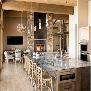 Cette image montre une grand cuisine américaine parallèle chalet avec des portes de placard en bois clair, un îlot central, un évier encastré, un placard à porte shaker, un électroménager en acier inoxydable, un sol beige, un plan de travail en quartz et un sol en bois brun.