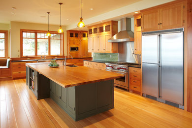 Inspiration for a large craftsman l-shaped light wood floor open concept kitchen remodel in Seattle with a farmhouse sink, shaker cabinets, light wood cabinets, wood countertops, green backsplash, ceramic backsplash, stainless steel appliances and an island