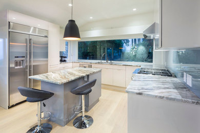 This is an example of a medium sized modern u-shaped kitchen/diner in Vancouver with a submerged sink, flat-panel cabinets, white cabinets, blue splashback, glass sheet splashback, stainless steel appliances, light hardwood flooring, an island, marble worktops and beige floors.